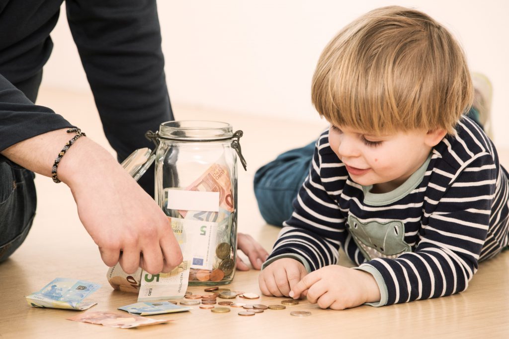 Malý chlapec s rodičom ukladajú peniaze do šporiacej sklenenej nádoby
